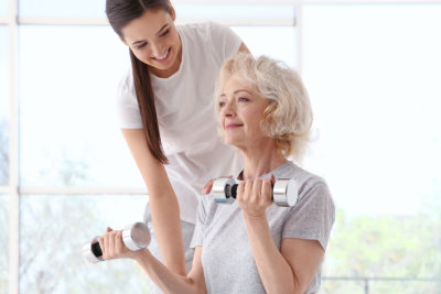 nurse assisting elderly woman doing dumbbell