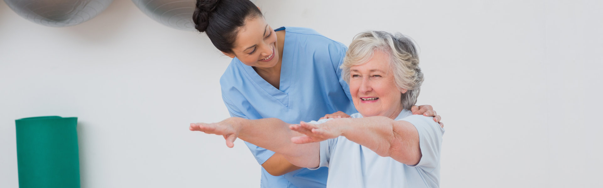 happy instructor assisting senior woman in exercising at gym